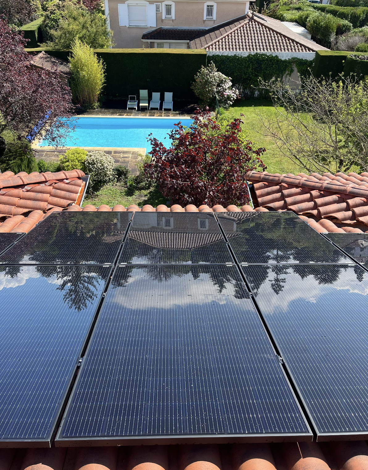 Panneaux solaires sur toit avec vue sur jardin et piscine bleue entourée de végétation