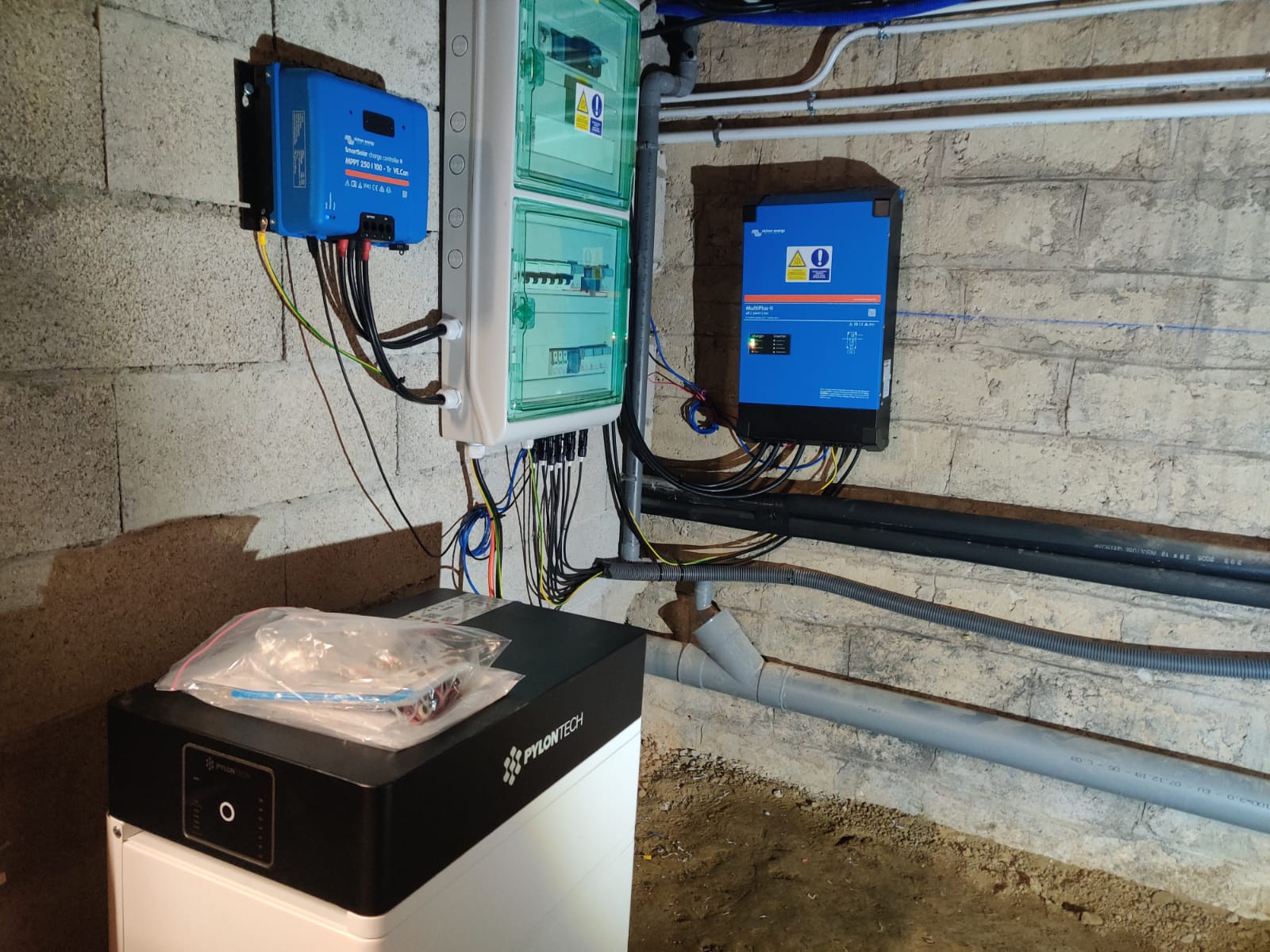 Installation électrique solaire avec onduleurs bleus, tableau électrique vert et batterie Pylontech dans un local technique