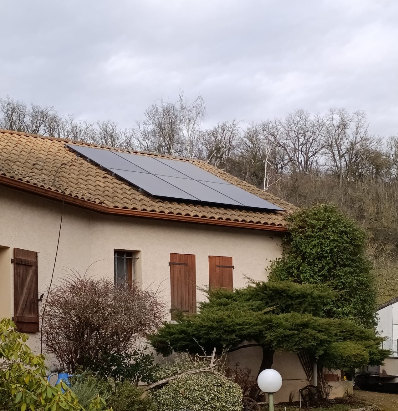 Maison avec panneaux solaires sur toit en tuiles et volets en bois dans un environnement boisé