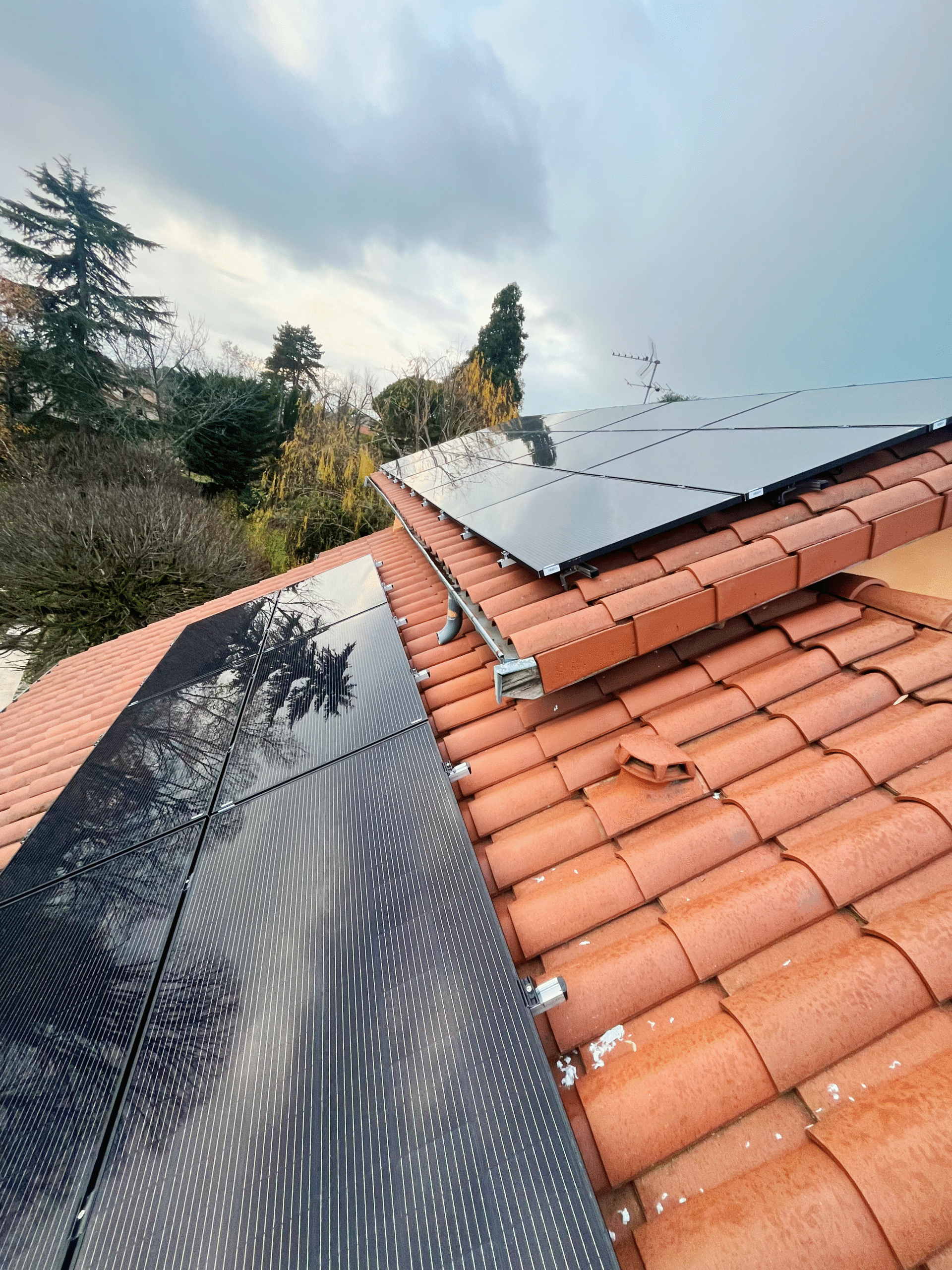 Panneaux solaires montés sur toiture en tuiles canal avec reflets d'arbres et ciel nuageux