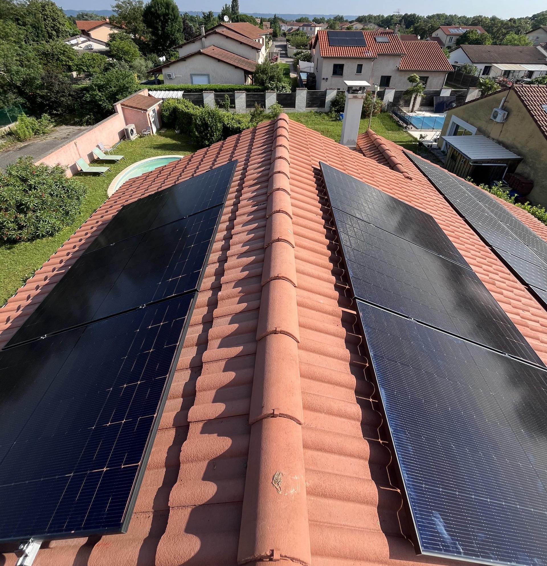 Vue aérienne d'un toit avec panneaux solaires sur tuiles rouges, quartier résidentiel avec piscines en arrière-plan