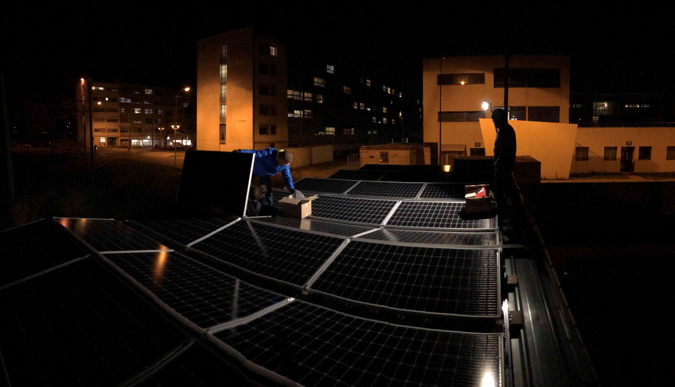 Installation de panneaux solaires de nuit sur toiture d'immeuble avec des techniciens Zest