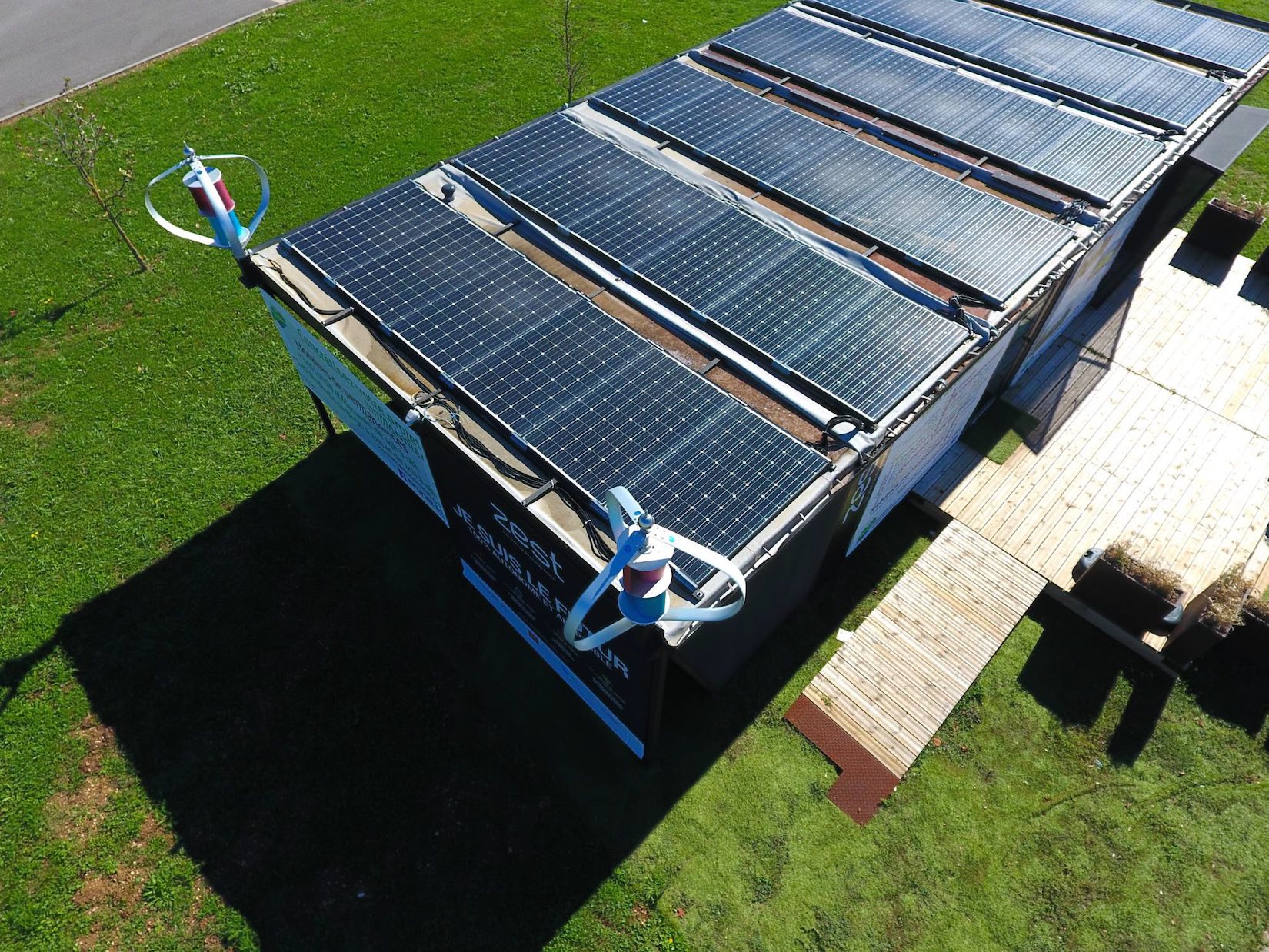 Vue aérienne de maison avec panneaux solaires et éolienne domestique dans le jardin