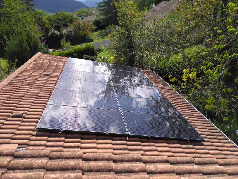 Panneaux solaires reflétant les nuages sur toit de tuiles, environnement boisé et montagneux