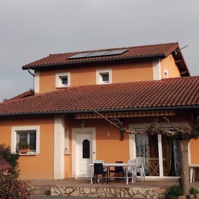 Maison orange avec toiture en tuiles équipée de panneaux solaires et terrasse avec mobilier de jardin
