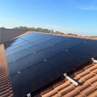 Panneaux solaires noirs installés sur un toit de tuiles en terre cuite sous un ciel bleu dégagé