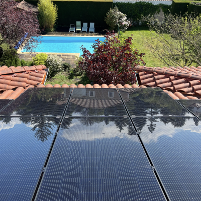 Panneaux solaires sur toit avec vue sur jardin et piscine bleue entourée de végétation