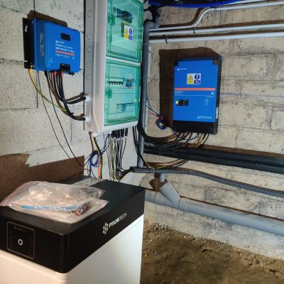 Installation électrique solaire avec onduleurs bleus, tableau électrique vert et batterie Pylontech dans un local technique