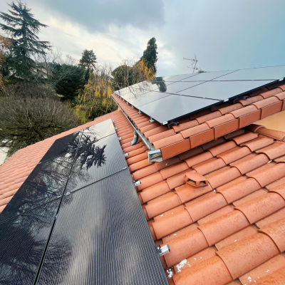 Panneaux solaires montés sur toiture en tuiles canal avec reflets d'arbres et ciel nuageux