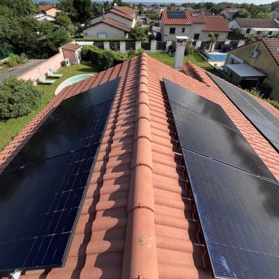 Vue aérienne d'un toit avec panneaux solaires sur tuiles rouges, quartier résidentiel avec piscines en arrière-plan