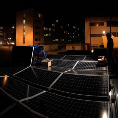Installation de panneaux solaires de nuit sur toiture d'immeuble avec des techniciens Zest