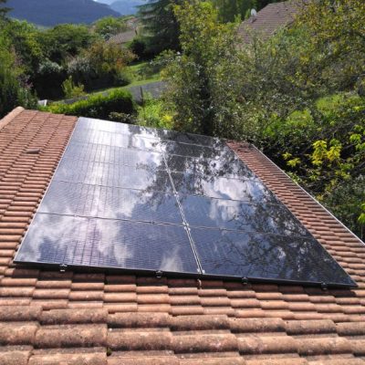 Panneaux solaires reflétant les nuages sur toit de tuiles, environnement boisé et montagneux